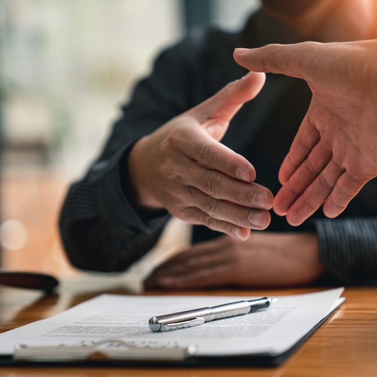 Two people reaching across table to shake hands