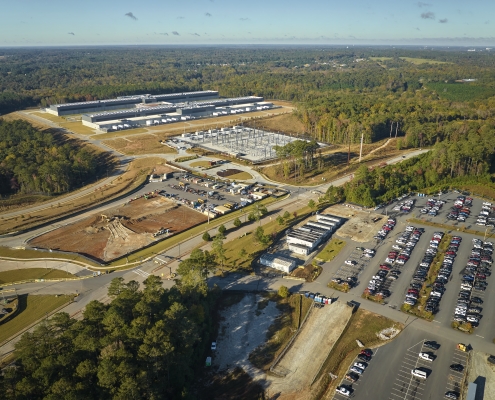 Many associate cars parked on big parking lot in front of industrial factory building. Manufactoring and global industry concept